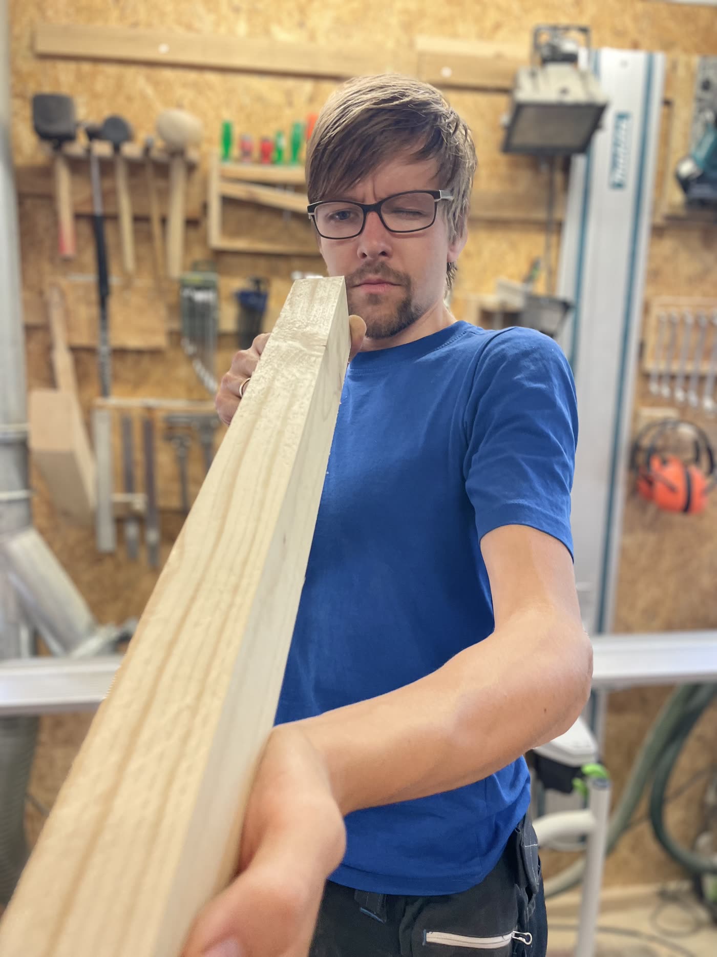 Johannes prüft in der Werkhalle ein langes Holzbrett